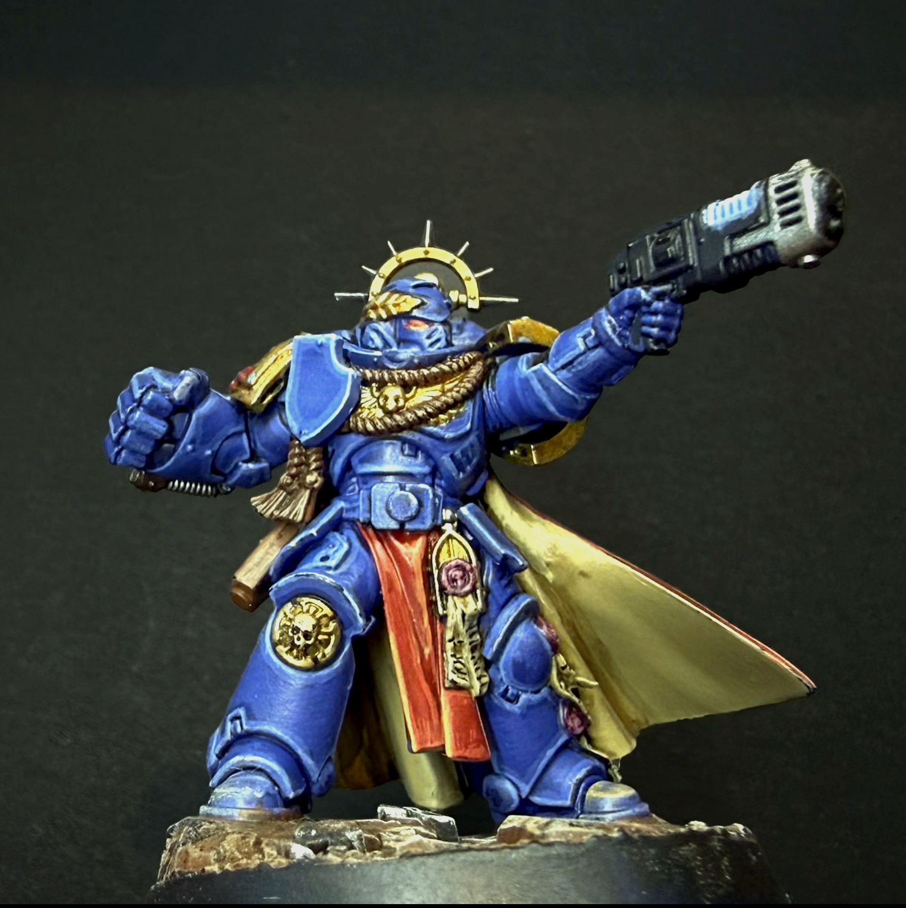 Painted Ultramarines Captain in blue and gold power armour with a golden laurel halo, pistol raised